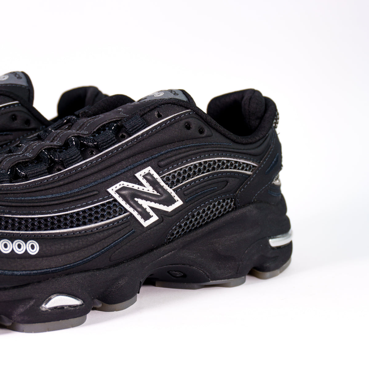 Боковина New Balance 1000 Lunar Pack зблизька: чорна N з перфорованим срібним контуром